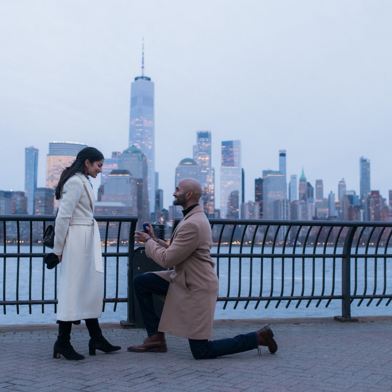 The Manhattan skyline behind them, a man kneels and proposes to his girlfriend. 