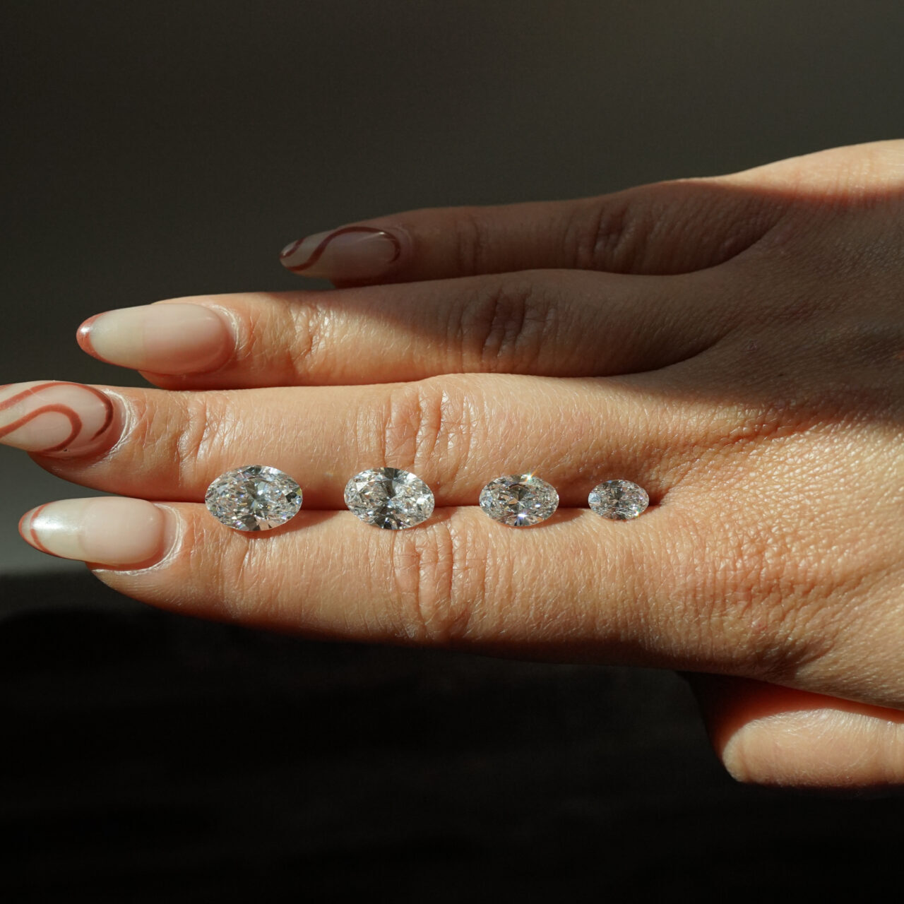 A hand displays four oval cut diamonds in various shapes