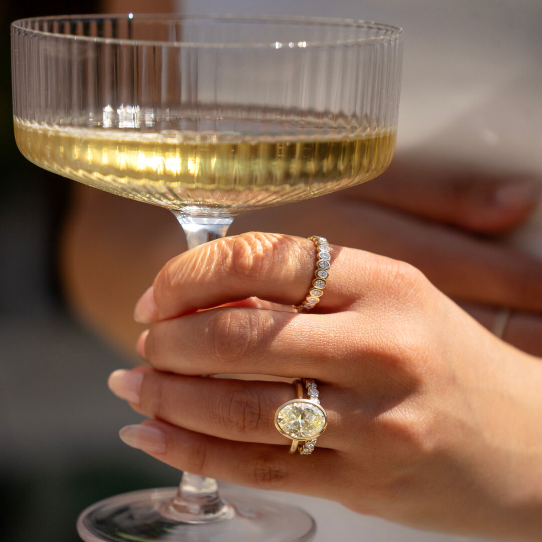 A woman holds a champagne glass and rocks multiple diamond rings 
