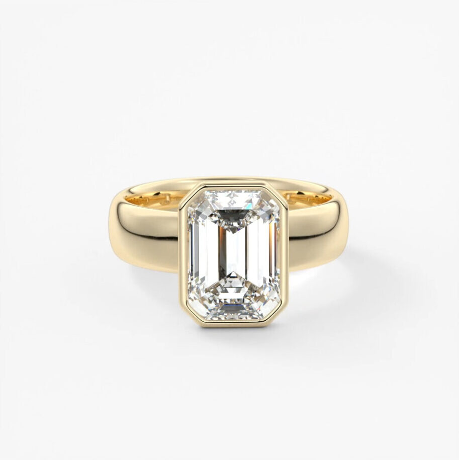 A bezel set emerald cut, lab grown engagement ring on a chunky, yellow gold band 