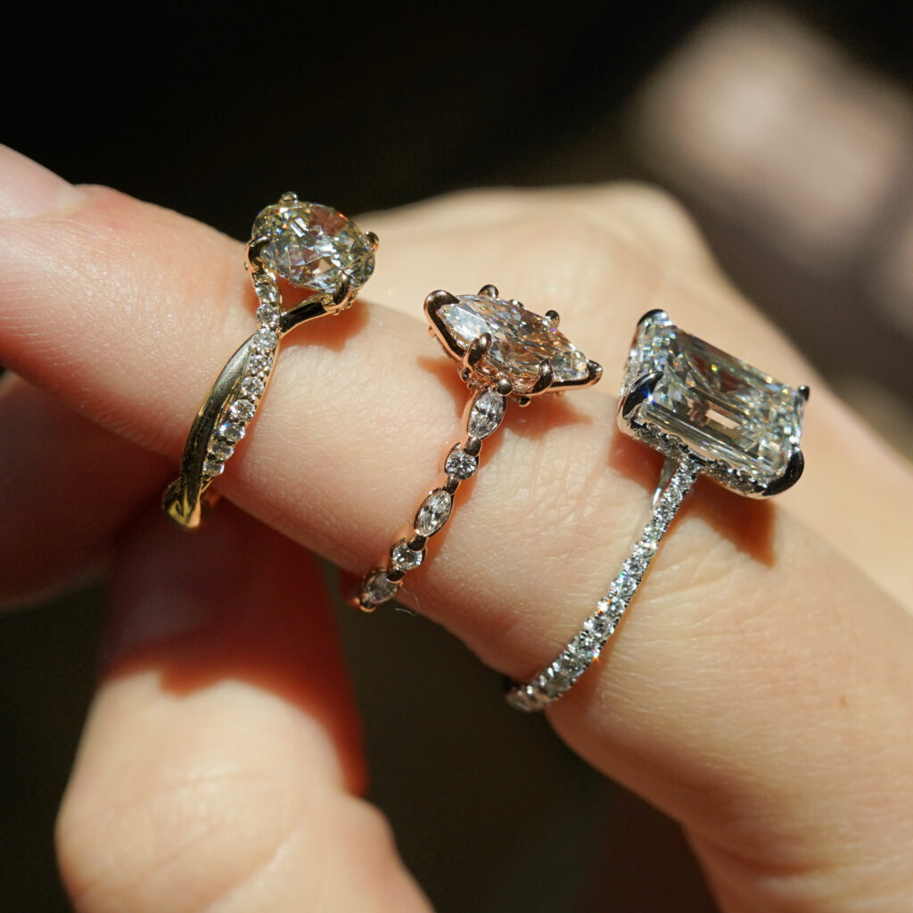 Three diamond engagement rings rest on a finger with various diamond details 