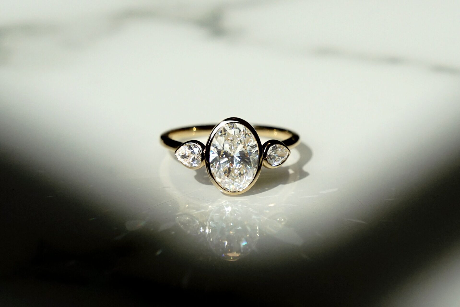 Two diamond shapes on one ring. A bezel set oval is surrounded by two smaller pear cut diamonds. 