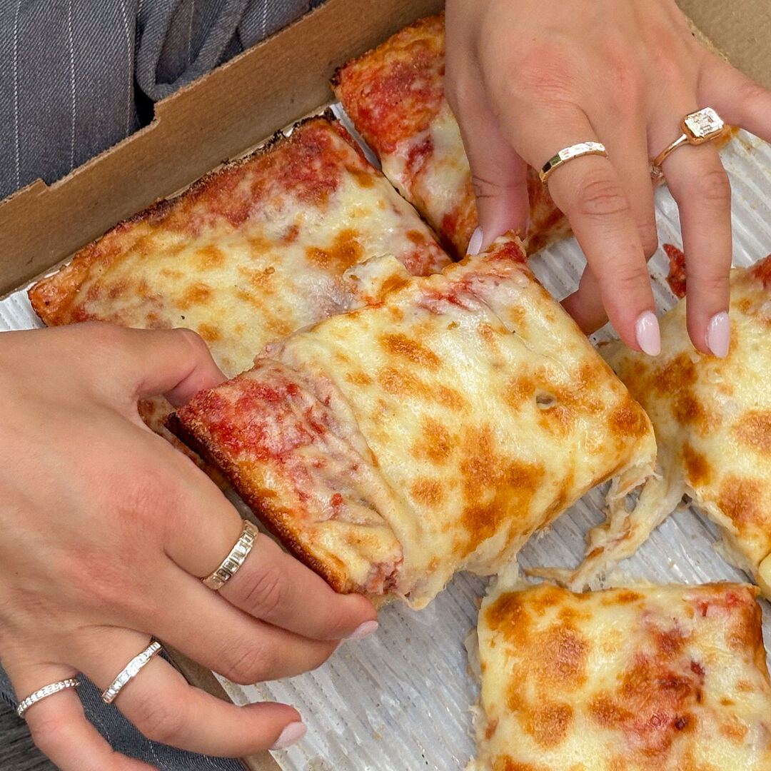 A woman holds a slice of pizza and wears a variety of lab grown diamond rings 