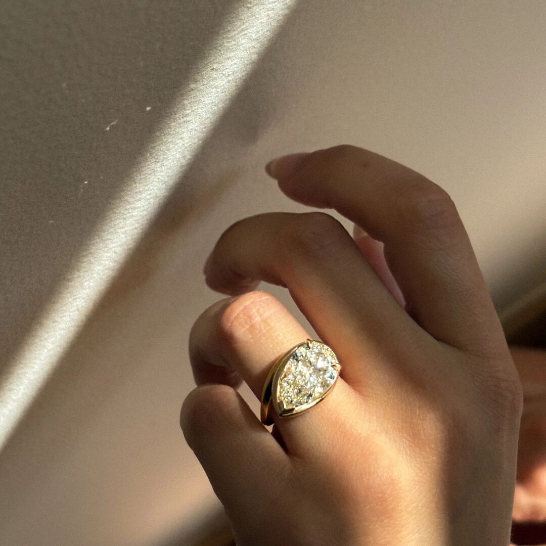 A pear cut, collet set engagement ring in front of a neutral background 
