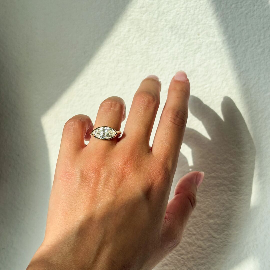 Woman wears an east west set Marquise diamond engagement ring in front of a white wall 